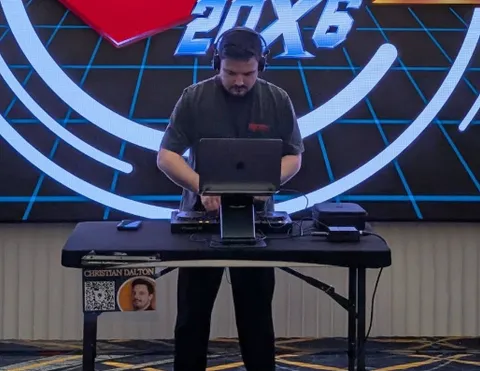 Christian Dalton performing at a table with a laptop in front of a screen showing retro game graphics.